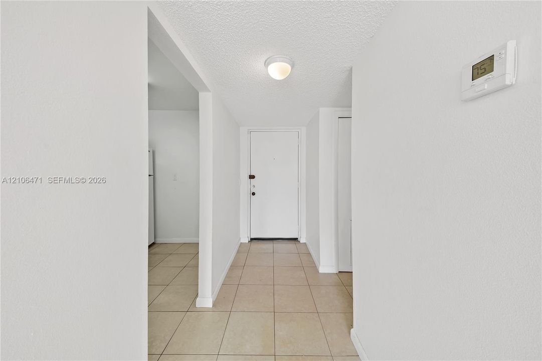 Neutral-toned tile flooring, solid-core entry door, ceiling-mounted flush lighting, and wall-mounted digital thermostat