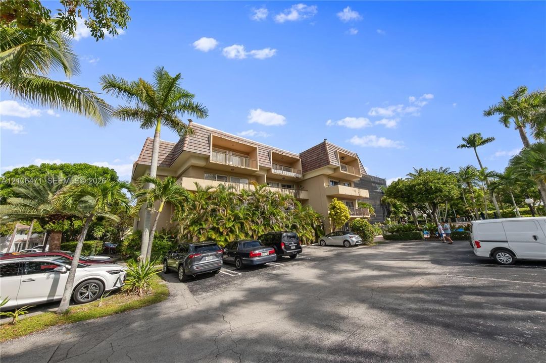 Multi-story exterior featuring a shingled mansard roofline, private balconies, and mature palm tree landscaping