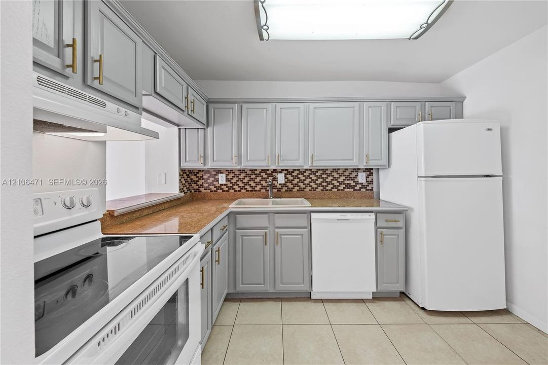 Kitchen featuring grey shaker-style cabinetry with gold-tone hardware, stone-finish countertops, decorative mosaic tile backsplash, double-basin sink, and ceramic tile flooring