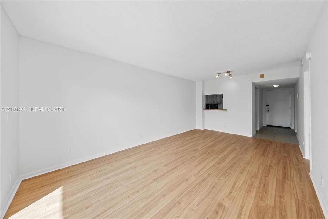 Open concept living area featuring wood-finish flooring, a pass-through serving window, recessed track lighting, and a tiled entryway