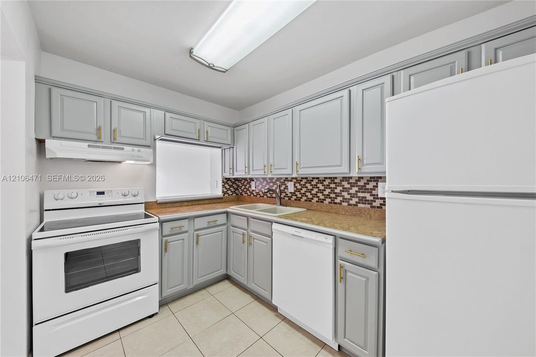 Kitchen featuring gray shaker-style cabinetry with gold-toned hardware, stone-finish countertops, a multi-tonal mosaic tile backsplash, and a double-basin sink