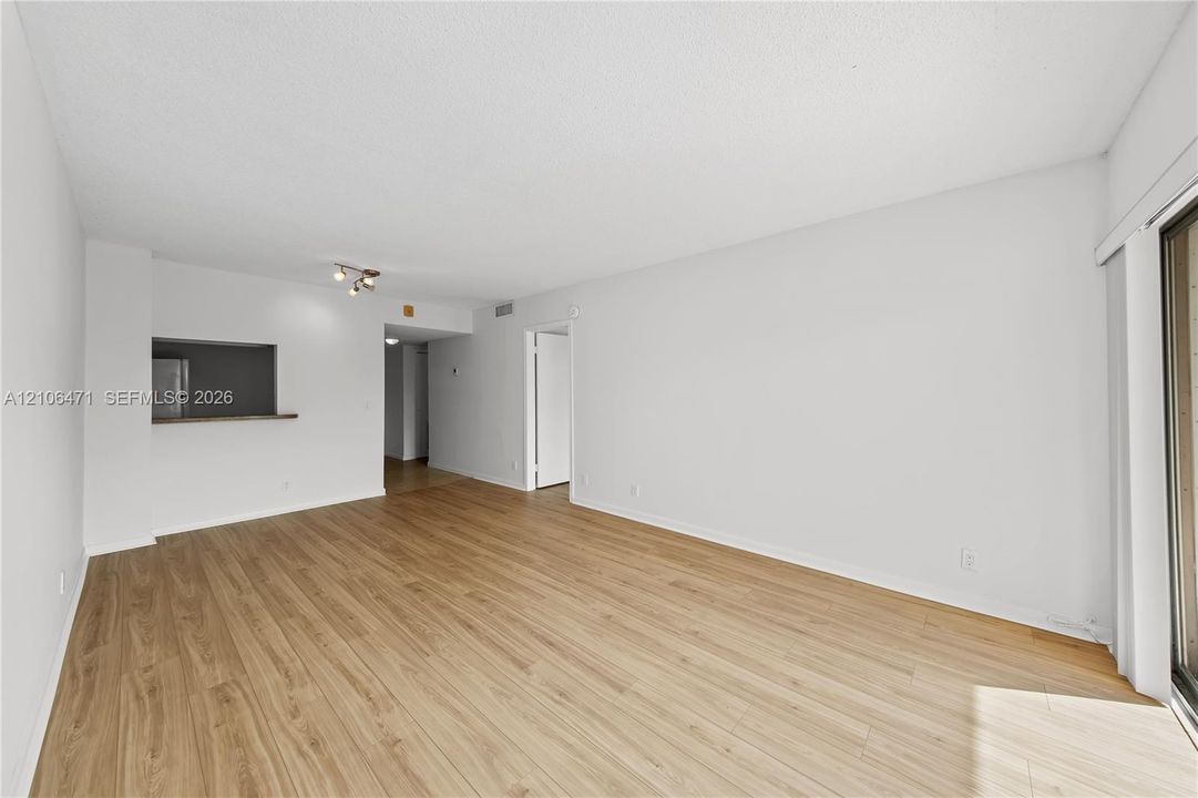 Neutral-toned living space featuring light wood-finish flooring, a pass-through opening, recessed lighting, and a sliding glass door