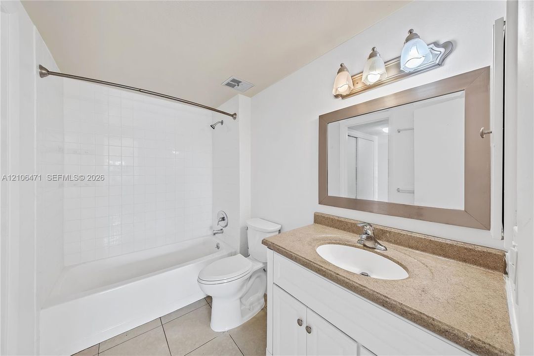Bathroom featuring a tub-shower combination with white tile surround, vanity with an integrated sink and stone-finish countertop, framed wall mirror, and tri-light fixture