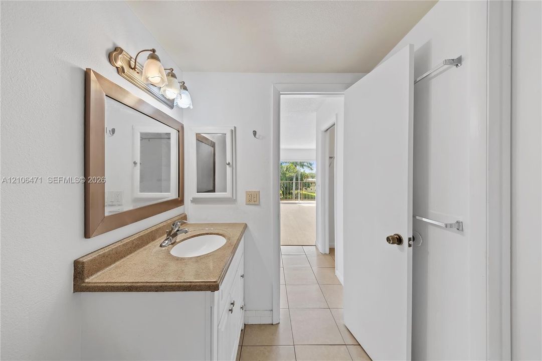 Bathroom featuring a vanity with integrated sink, stone-finish countertop, three-light fixture, framed mirror, and tiled flooring