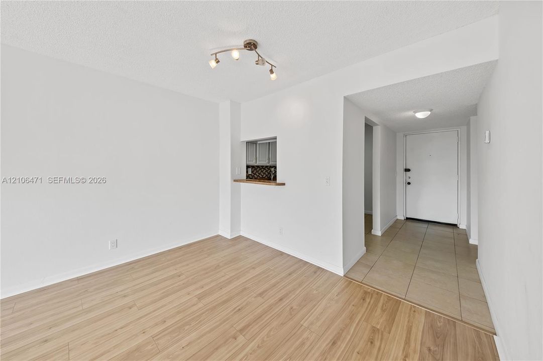 Wood-finish flooring, kitchen pass-through window, and ceramic tile entryway with a flush-mount light fixture