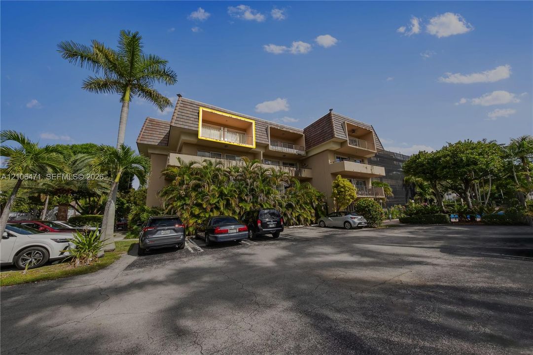 Multi-story residential building featuring a textured facade, mansard-style roof, private upper-level balconies, and mature palm tree landscaping