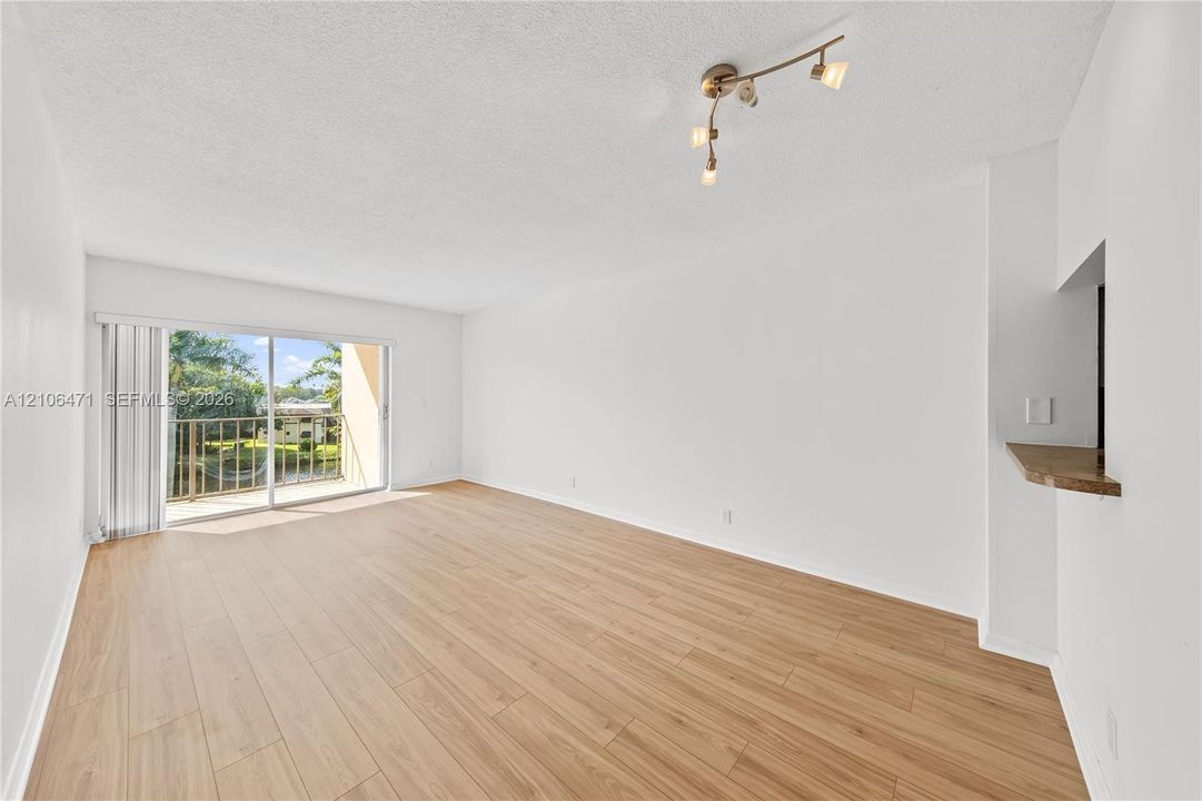 Open-concept interior featuring wood-finish flooring, sliding glass doors to a balcony, and a built-in pass-through ledge