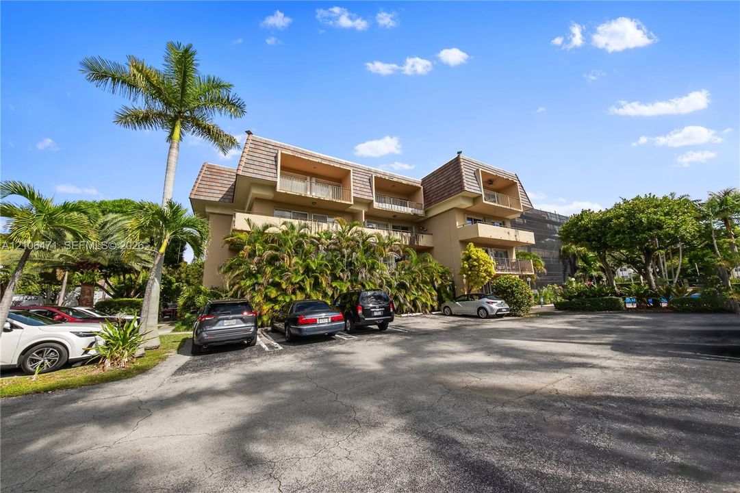 Multi-story residential building exterior featuring a mansard roofline, private balconies, and mature palm landscaping