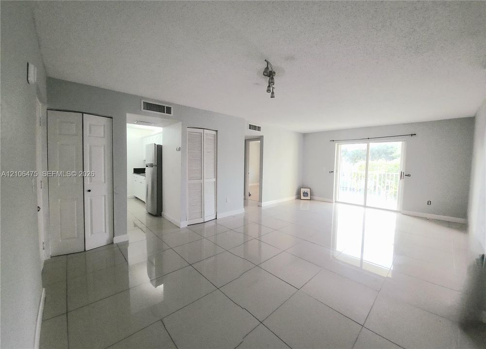 Large-format tile flooring, sliding glass doors, built-in louvered-door closets, and a central light fixture