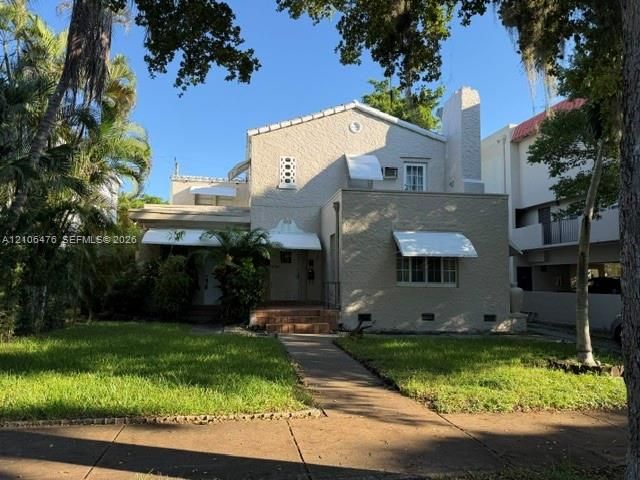 Stucco exterior residence featuring a tiled chimney, decorative geometric window accents, metal window awnings, and a brick-stepped entryway