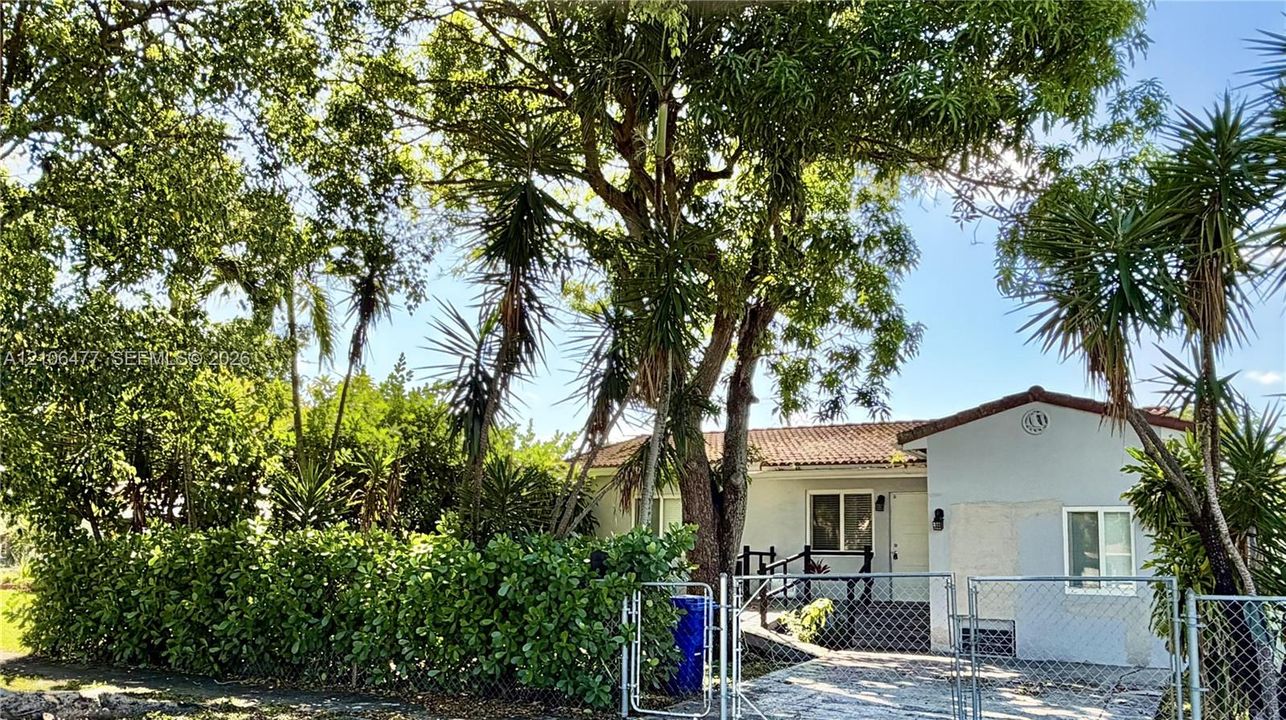 Single-story residence featuring a tile roof, stucco exterior, paved driveway, chain-link fencing, and mature landscaping
