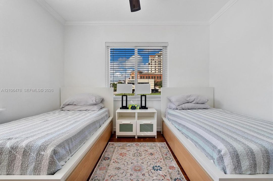 Room featuring wood-finish flooring, a central window with slatted blinds, and a ceiling-mounted fan