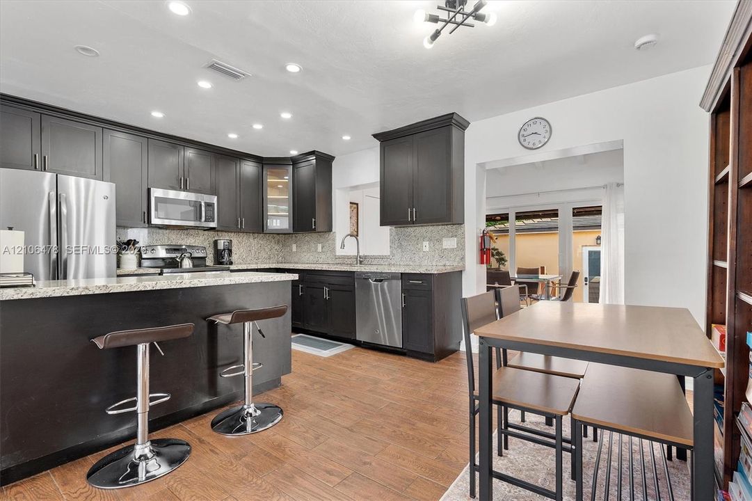 Kitchen featuring dark cabinetry, stone-surface countertops, stainless steel appliances, wood-finish flooring, and recessed lighting