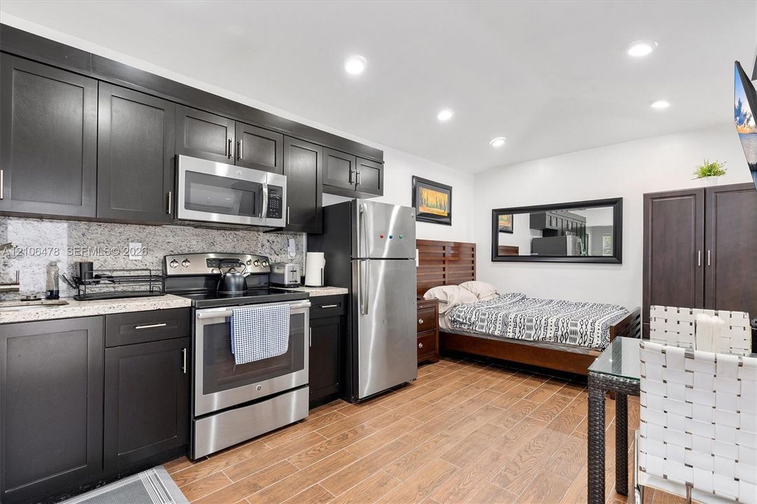 Kitchen featuring dark-finish cabinetry, stone countertops, stainless steel appliances, and wood-finish tile flooring with recessed lighting