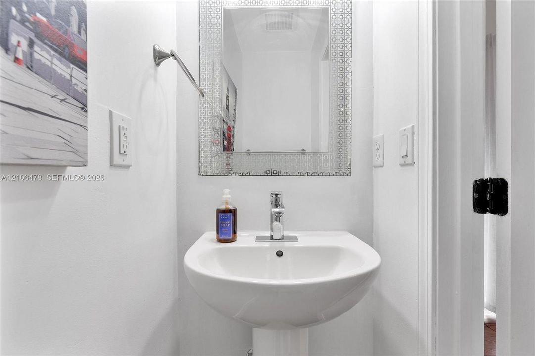 White pedestal sink with a chrome single-handle faucet and a decorative rectangular wall-mounted mirror
