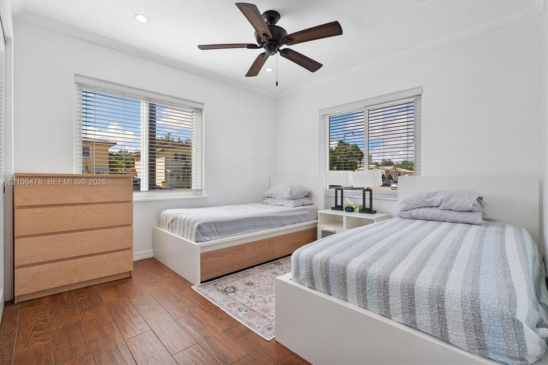 Room featuring wood-finish flooring, recessed lighting, crown molding, and a dark-finish ceiling fan, with dual windows providing natural light