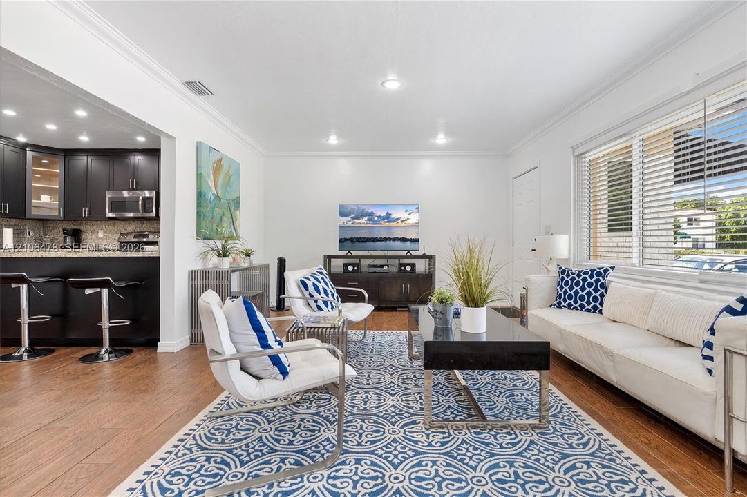 Open-concept living space featuring wood-finish flooring, recessed lighting, crown molding, and large windows with horizontal blinds