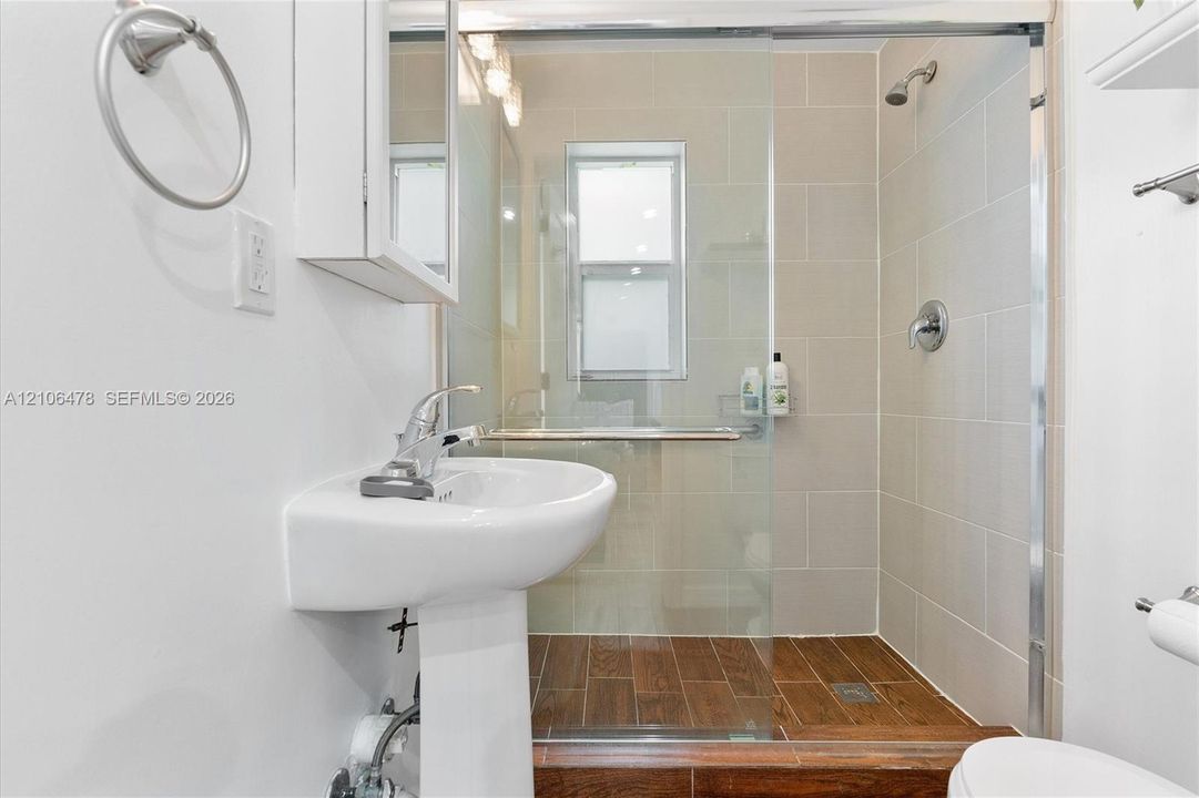Bathroom featuring a pedestal sink, a glass-enclosed shower with tiled walls, and wood-finish flooring