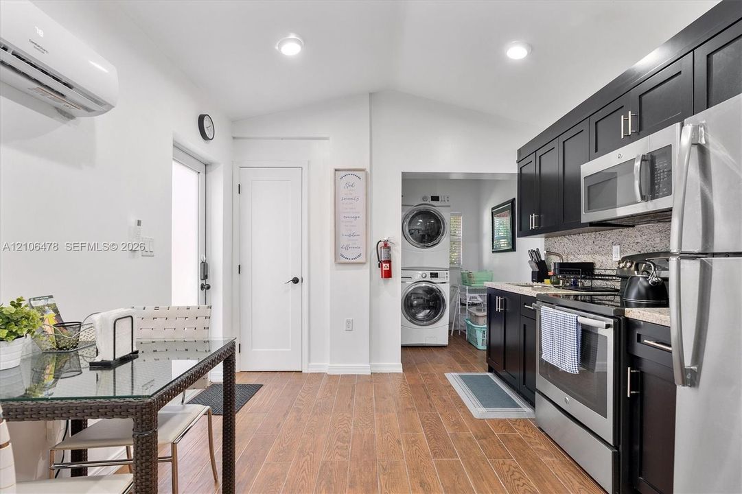Kitchen featuring dark-finish cabinetry, stainless steel appliances, speckled stone-surface countertops, wood-finish flooring, and a vaulted ceiling with recessed lighting