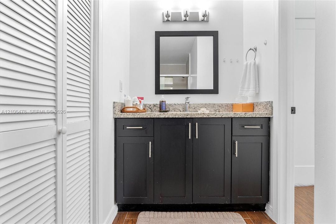 Bathroom vanity featuring dark-finished cabinetry, a speckled stone countertop, an integrated sink, a framed square mirror, and louvered closet doors