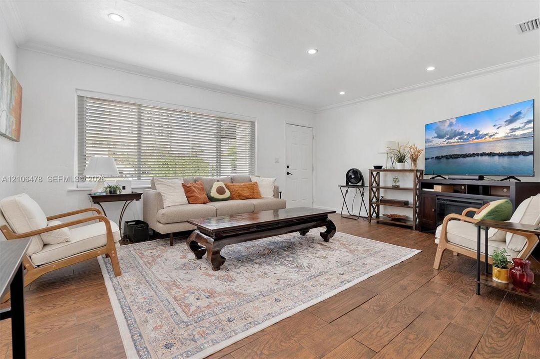 Living area featuring wood-finish flooring, recessed lighting, and expansive horizontal window with integrated blinds