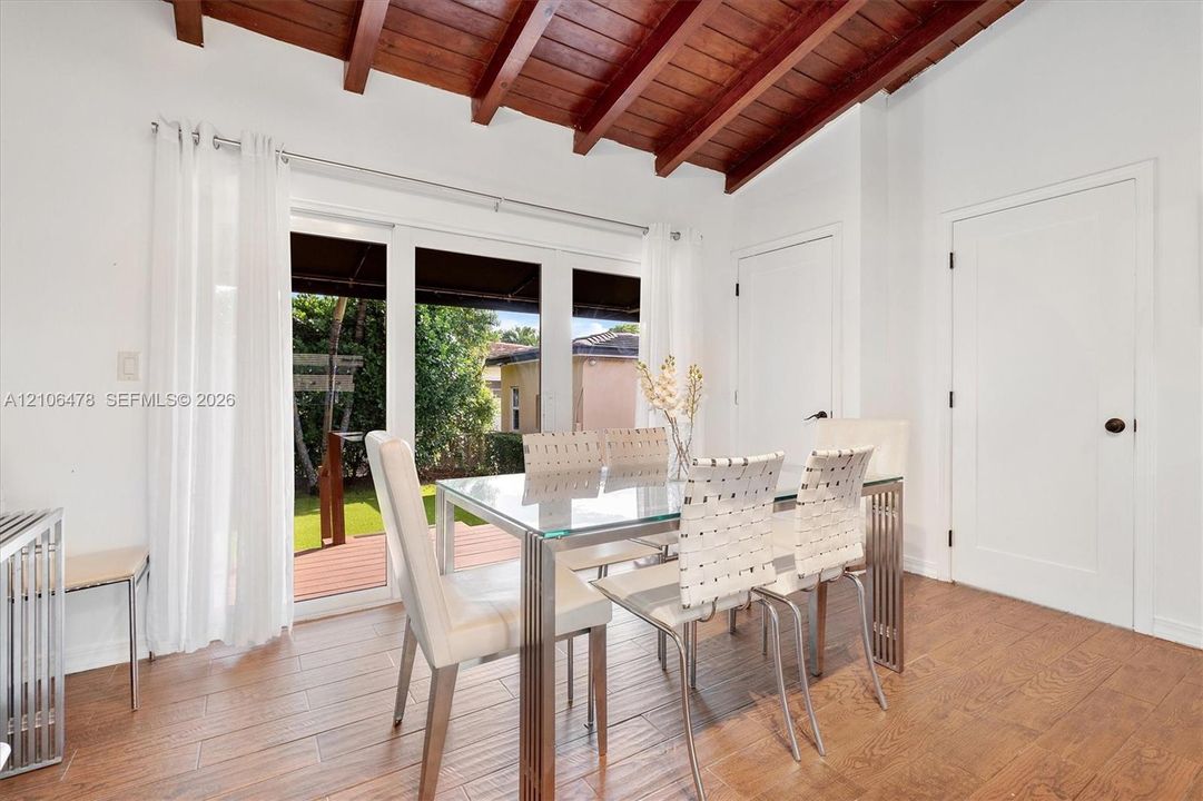 Vaulted ceiling with exposed wood beams, wood-finish flooring, and expansive glass sliding doors