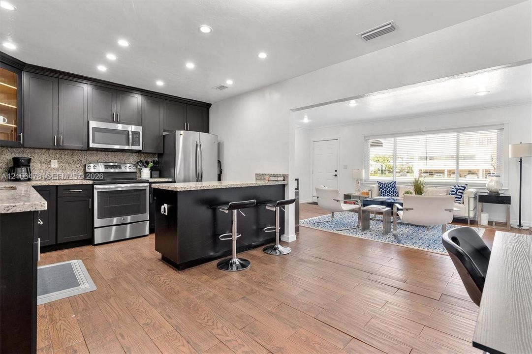 Kitchen featuring dark cabinetry, stone-surface countertops, stainless steel appliances, a center island with breakfast bar seating, and wood-finish flooring