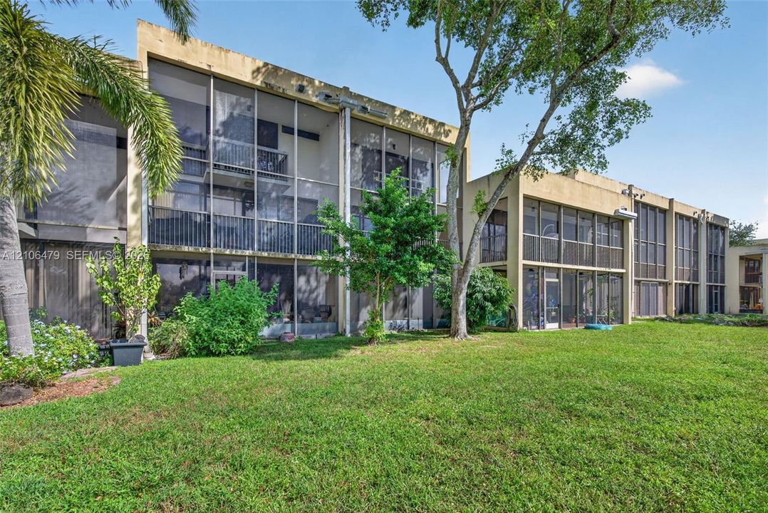 Multi-level exterior featuring screened-in lanais, stucco facade, and established landscaping including mature palms and shade trees
