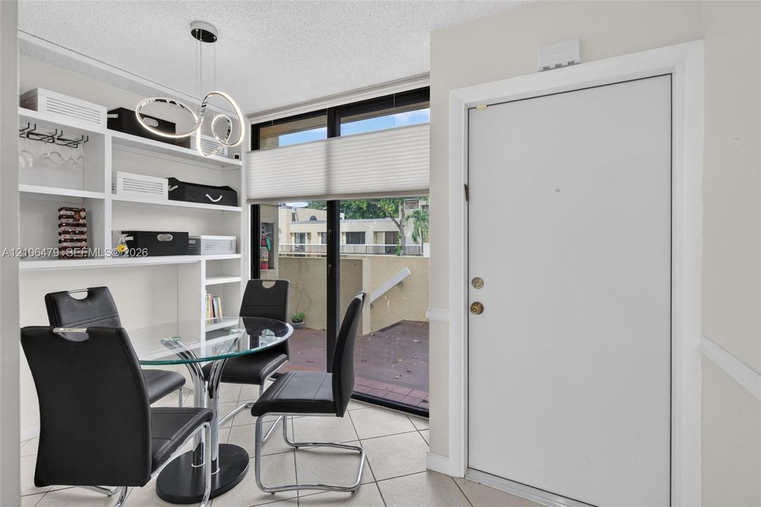 Built-in white shelving, tile flooring, contemporary multi-ring pendant lighting, and large sliding glass door with external patio access