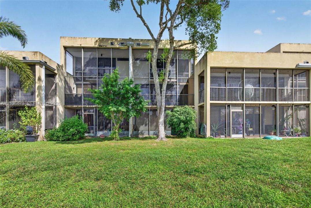 Exterior facade featuring multi-level screened-in lanais, metal railing systems, flat roof architecture, and an expansive lawn with mature landscaping