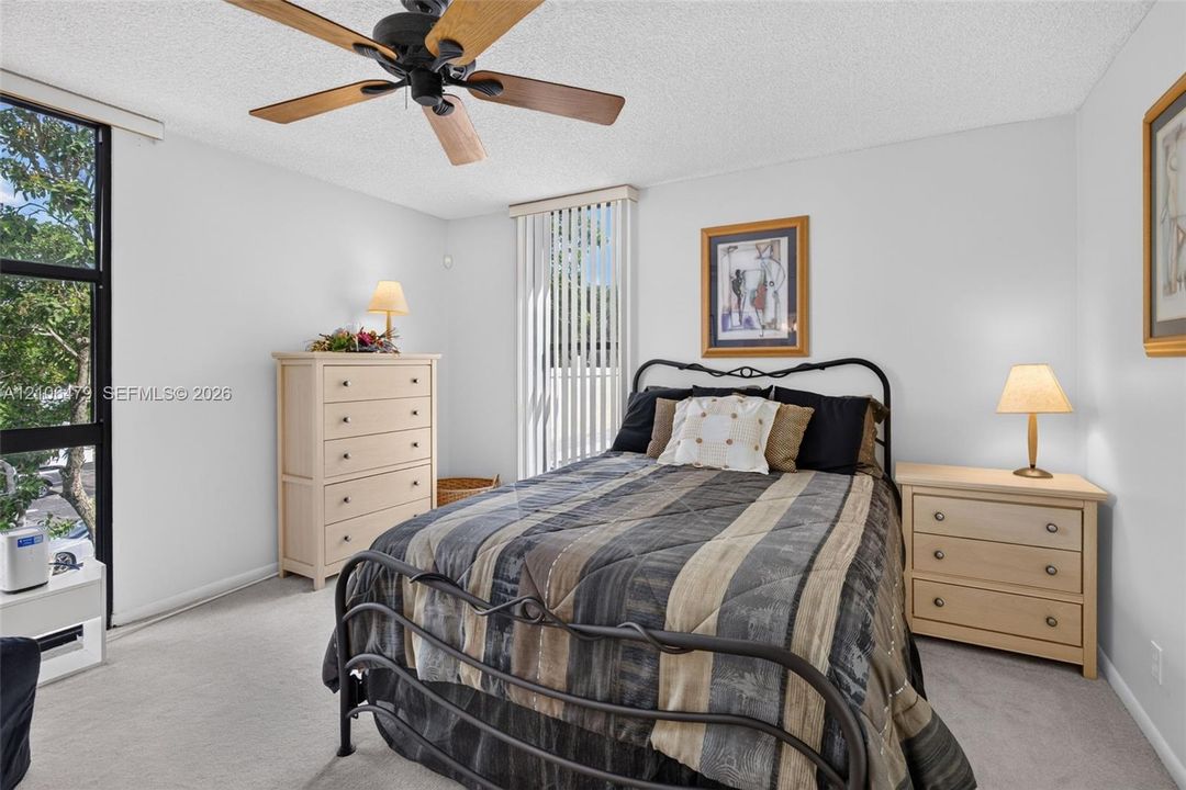 Interior space featuring neutral carpeting, a black-finished ceiling fan with wood-toned blades, floor-to-ceiling black-framed windows, and vertical blinds