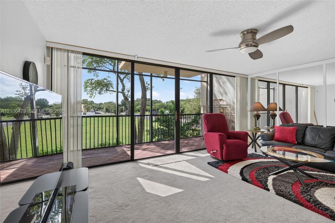 Floor-to-ceiling sliding glass doors opening to a screened balcony, mirrored wall panels, and a central ceiling fan