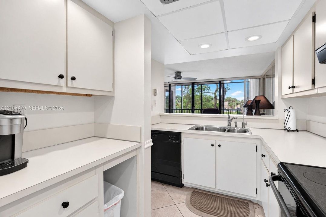 Kitchen featuring solid-surface countertops, white cabinetry, a dual-basin stainless steel sink, recessed ceiling lighting, and ceramic tile flooring