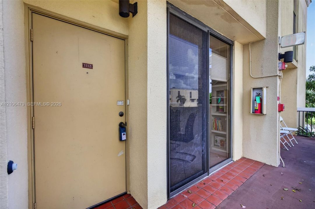 Exterior entryway featuring a solid-core door, sliding glass door with screen, stucco exterior wall finish, and tiled flooring