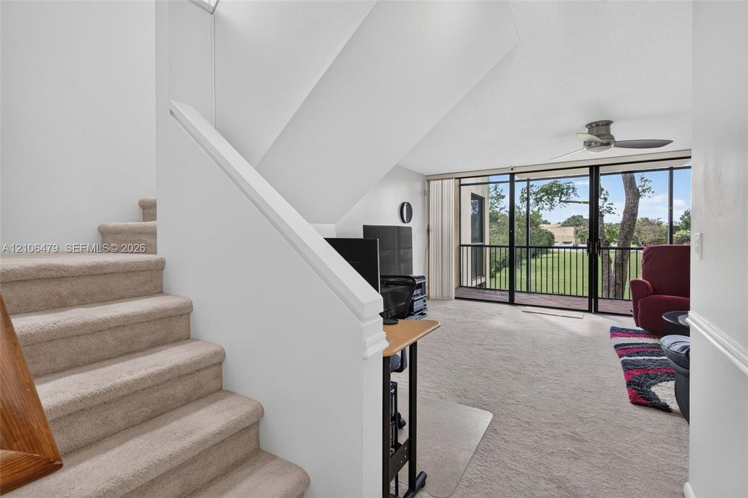 Carpeted staircase featuring a painted wood railing, wall-to-wall carpeting, ceiling fan, and sliding glass doors with balcony access