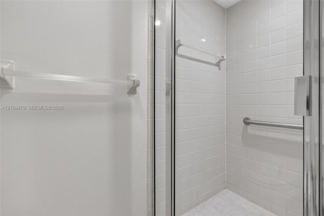 Shower enclosure featuring white wall tiling, a glass door, a wall-mounted metal grab bar, and a horizontal towel rack