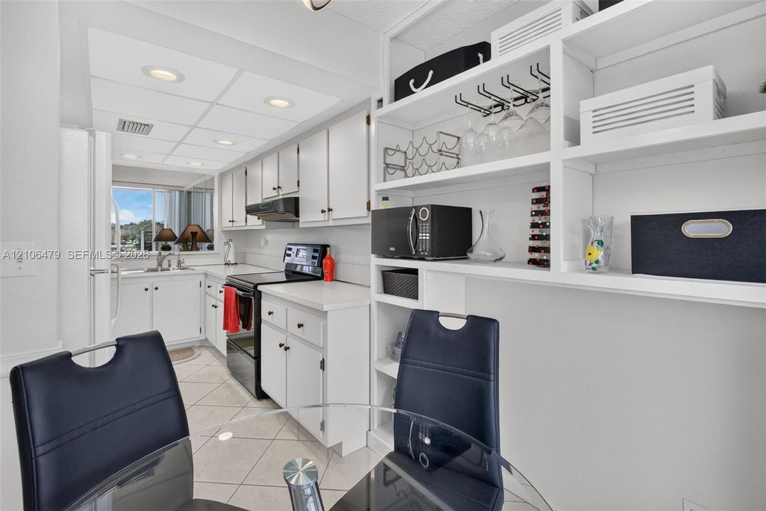 Kitchen featuring white shaker-style cabinetry, solid-surface countertops, tile flooring, recessed lighting, and built-in open display shelving