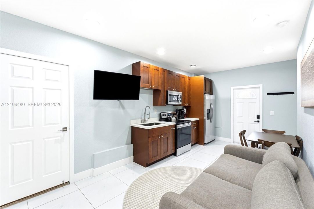 Kitchenette featuring wood-finish cabinetry, solid-surface countertops, a stainless steel electric range, a stainless steel microwave, and large-format tile flooring