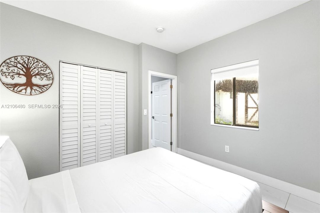 Interior space featuring neutral wall paint, white louvered-style closet doors, an interior panel door, and a single-pane window with a roller shade