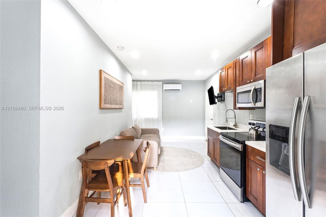 Kitchen featuring cherry-toned cabinetry, stainless steel appliances, a gooseneck faucet, tile flooring, and a wall-mounted climate control unit