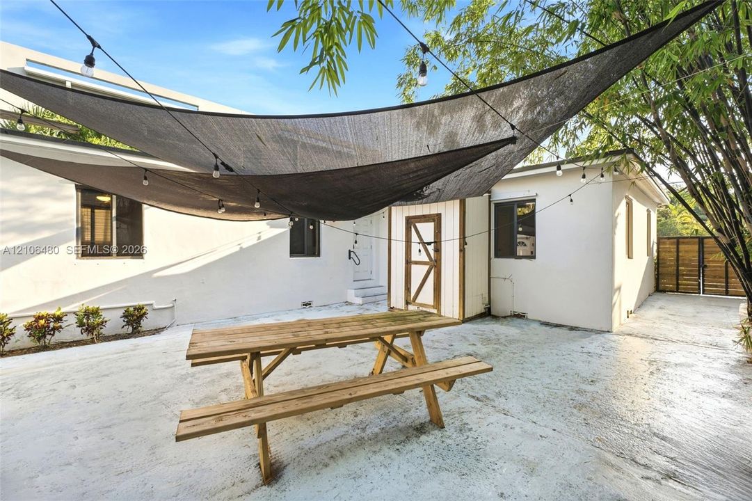 Outdoor patio featuring a concrete surface, overhead tension shade sails, exterior string lighting, and wood privacy fencing