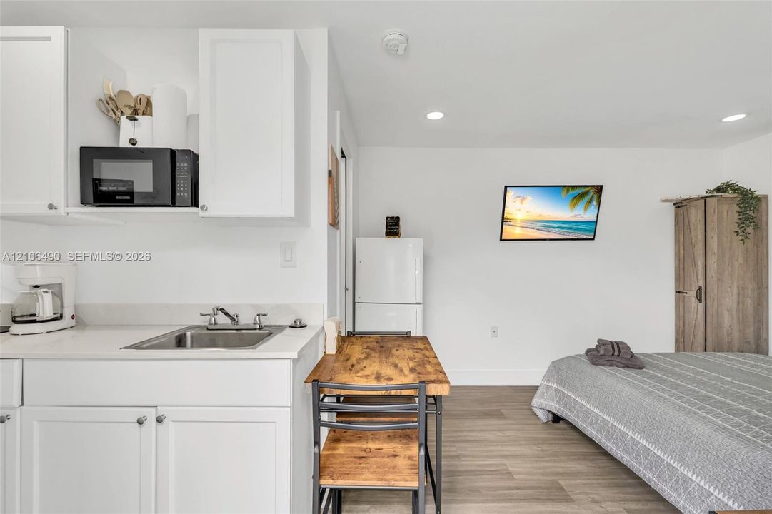 Kitchenette featuring white cabinetry, a stainless steel sink, solid-surface countertop, and recessed lighting with wood-finish flooring