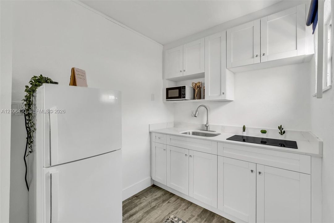 Kitchenette featuring white Shaker-style cabinetry, white countertops, built-in electric cooktop, stainless steel sink with high-arc faucet, and wood-finish flooring