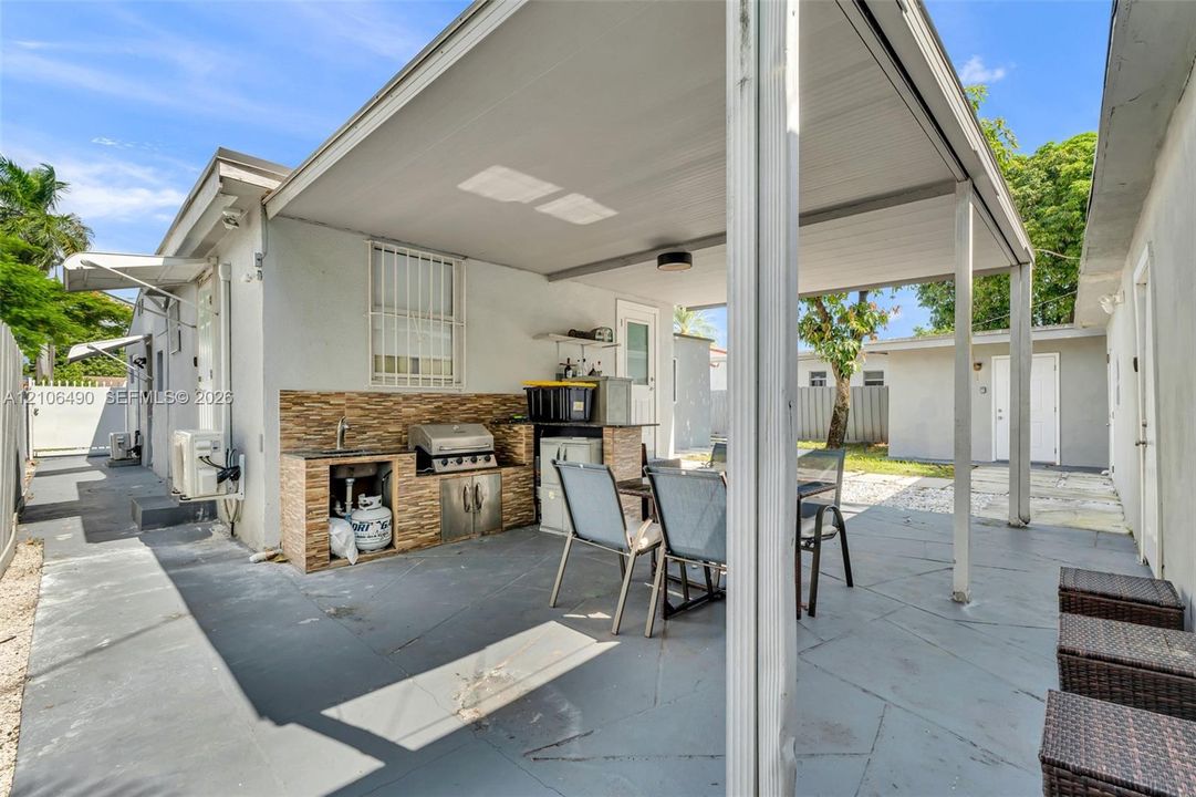 Covered patio featuring a built-in outdoor kitchen with stone-finish tiling, a stainless steel grill, a sink, and concrete flooring
