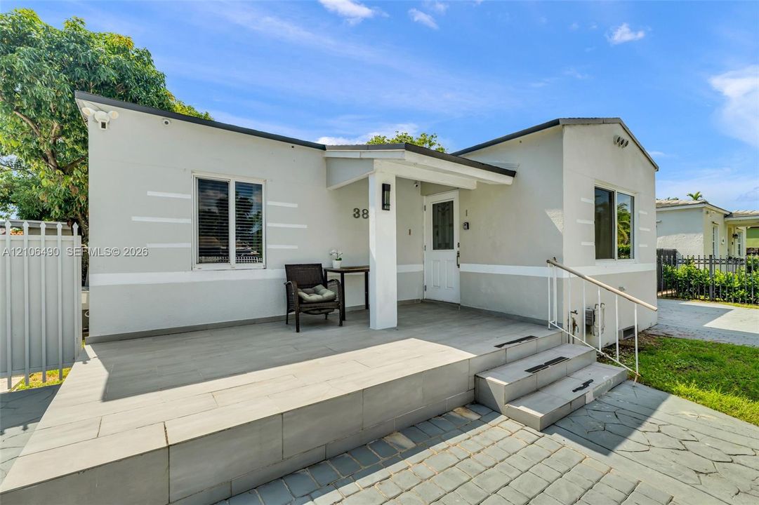 Exterior featuring a covered porch with large-format tile flooring, a white paneled front door, horizontal accent trim, and a stone paver walkway