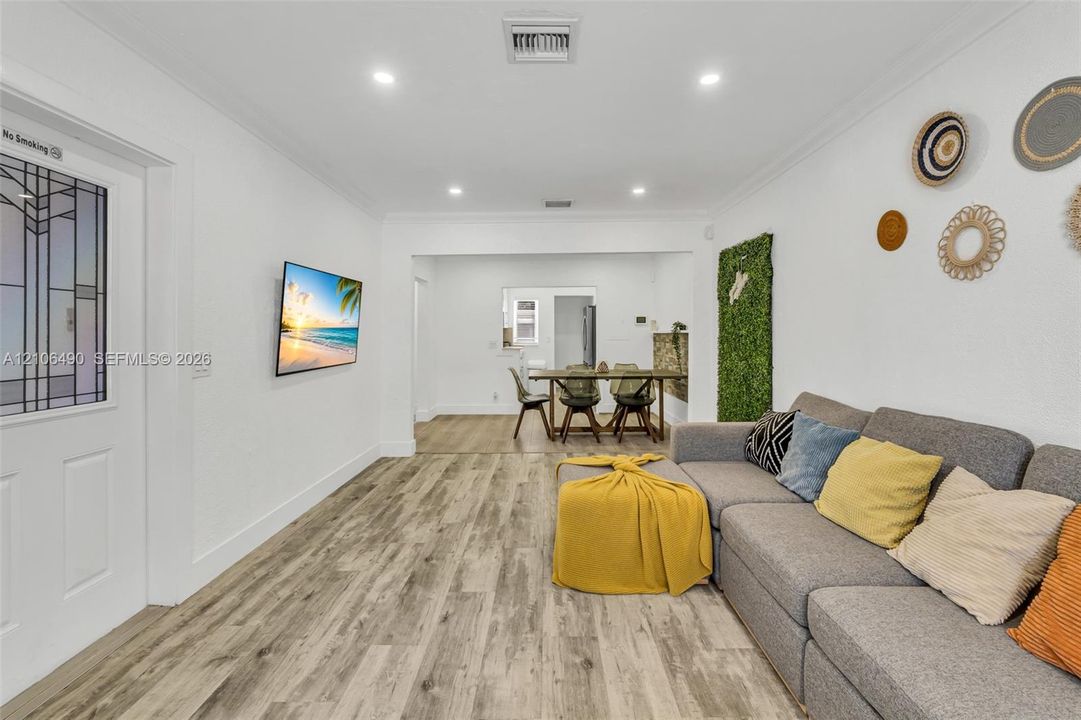 Open-concept interior featuring wood-finish flooring, recessed lighting, crown molding, and a decorative door with a leaded glass insert