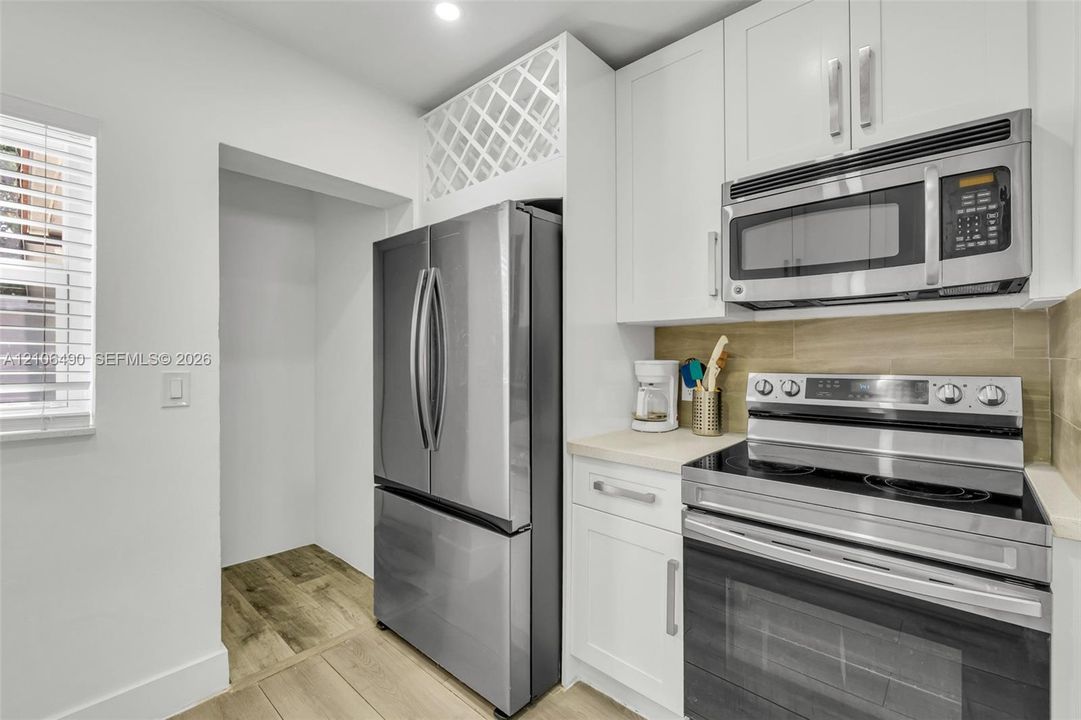 Kitchen featuring white shaker-style cabinetry, stainless steel appliances, built-in wine storage, wood-finish flooring, and a rectangular tile backsplash