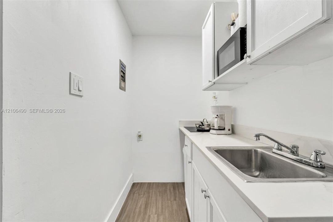 Kitchenette area featuring white cabinetry, solid-surface countertops, an undermount stainless steel sink, and wood-finish flooring