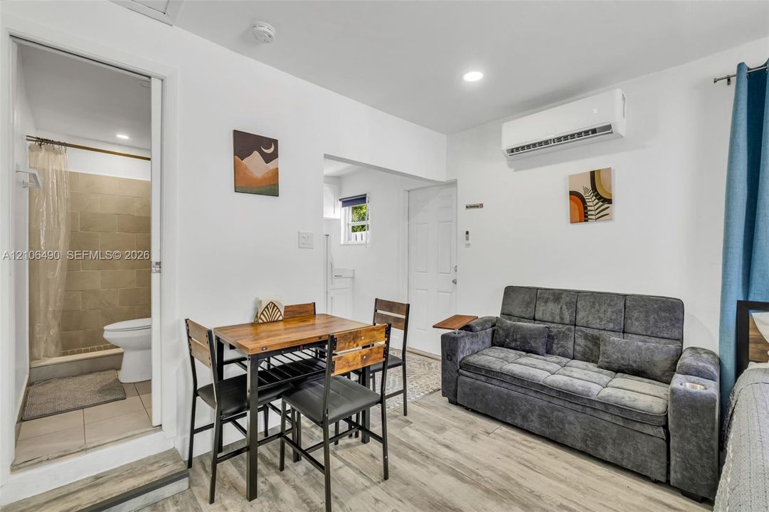 Wood-finish flooring, wall-mounted ductless air conditioning unit, recessed lighting, and a bathroom featuring a walk-in shower with neutral tile surround