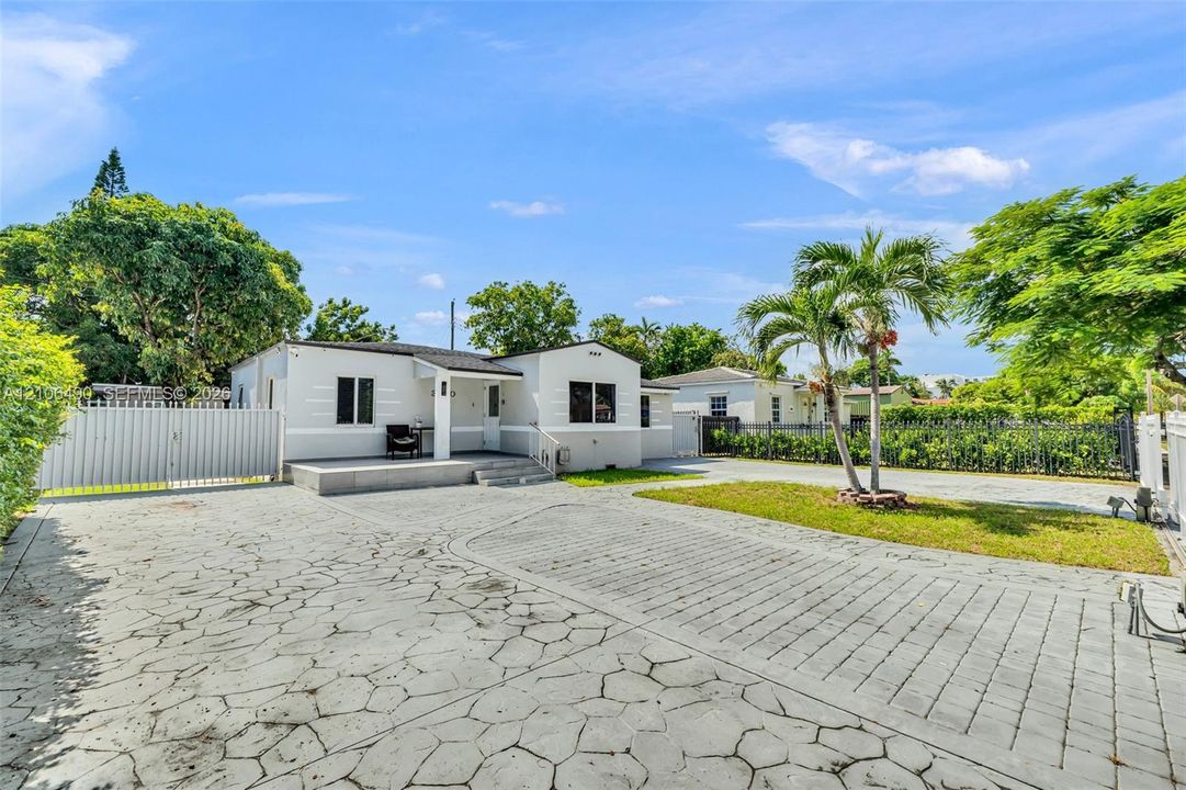 Single-story exterior featuring light-toned masonry, expansive patterned paver driveway, front concrete patio, and gated perimeter fencing